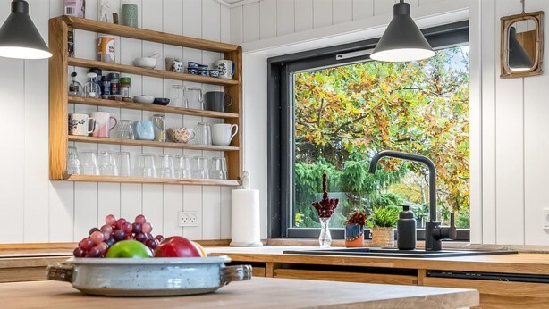 Eine Küche mit Holzböden, einem Fenster mit Blick auf Bäume und einer Obstschale auf der Arbeitsfläche.