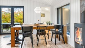 Ein moderner Essbereich mit Holztisch und schwarzen Stühlen, einer Pendelleuchte und einem Kamin.