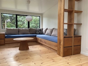 A modern room with a built-in bench seating area, a round wooden table, and a large window with a view of greenery. - "Sofija" -  from the sea by Interhome (Hals)