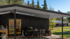 Ein überdachter Außenbereich mit Tisch, Stühlen, Grill und Blick auf ein bewaldetes Gebiet.