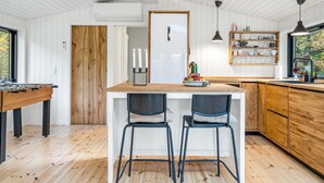 Eine moderne Küche mit einer Holztheke, zwei Barhocker, Pendelleuchten und Blick ins Freie.
