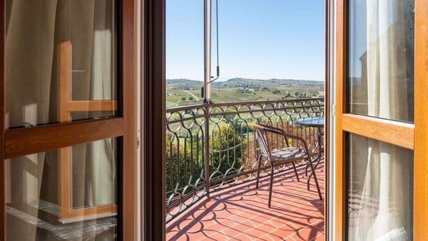 Un balcón con vista a un paisaje rural, una baranda de metal y una silla.