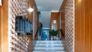Un pasillo moderno con paredes de ladrillo, una vitrina de vidrio, una planta en maceta y una escalera que sube a otro nivel.