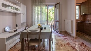Una cocina moderna con armarios blancos, un comedor con piso de mármol y vistas a un área exterior a través de una puerta de vidrio.