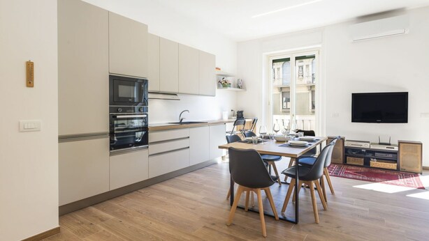 Una cocina moderna con electrodomésticos integrados, un comedor con mesa y sillas de madera, y un televisor de pantalla plana montado en la pared.