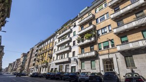 Una hilera de edificios de varios pisos con balcones, coches estacionados y un cielo azul despejado.