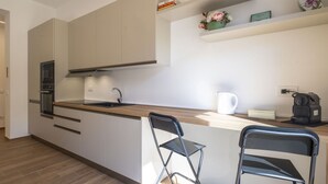 Una cocina moderna con horno integrado, pileta y cafetera. Hay dos sillas y una estantería con objetos decorativos.
