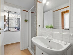 Een badkamer met een wit wastafel, een spiegel en een douchehoek.