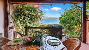 A wooden table set for dining with a view of the sea and mountains. - Beautiful apartment for 6 people with pool, WIFI, A/C, TV and patio (La Maddalena)