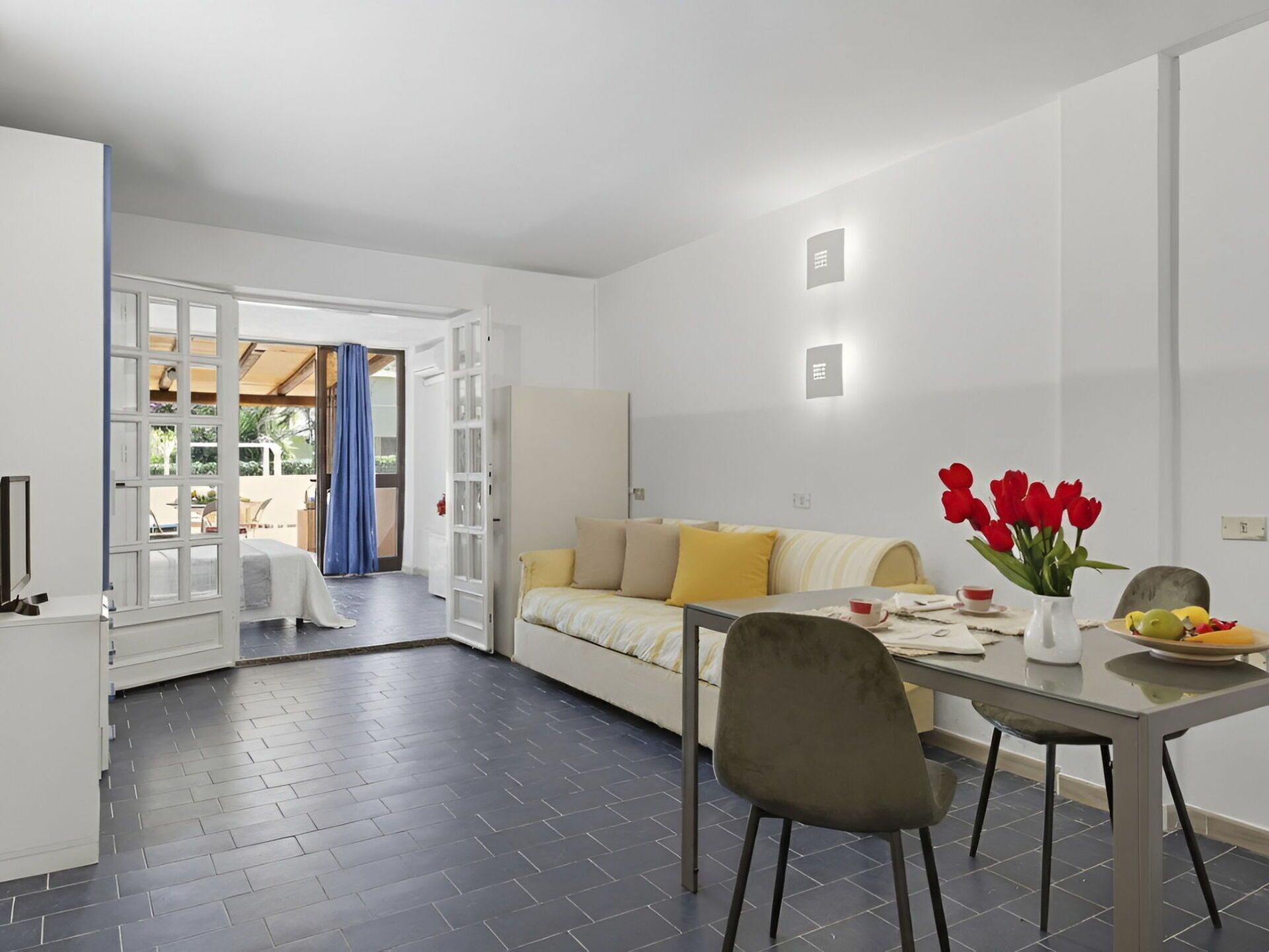 Uma sala de estar moderna com um sofá, uma mesa de jantar com cadeiras e um vaso com flores vermelhas.
