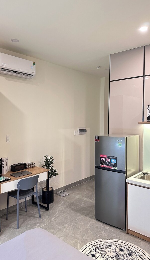 A compact kitchen with a refrigerator, a built-in oven, a small countertop, and a chair.