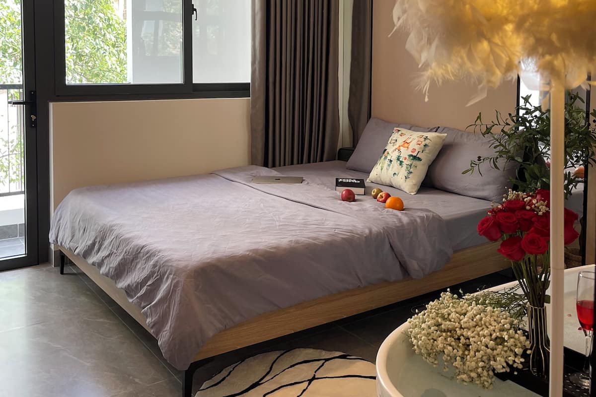 A modern bedroom with a bed, a large window, a potted plant, and a vase with flowers.