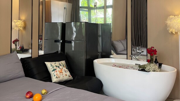 A modern bedroom with a bed, a large mirror, a bathtub, and a kitchen area visible through the mirror. - Unite StayCation Le Van Sy (Ho Chi Minh City)