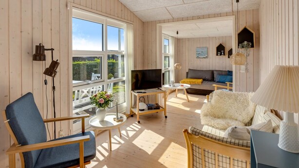 Un vaste espace de vie avec des murs en bois, une grande fenêtre, un canapé, un téléviseur et une table agrémentée d’un vase de fleurs.