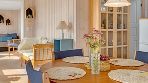 Un coin repas avec une table en bois, des sets de table en fibres tressées et un vase rempli de fleurs.