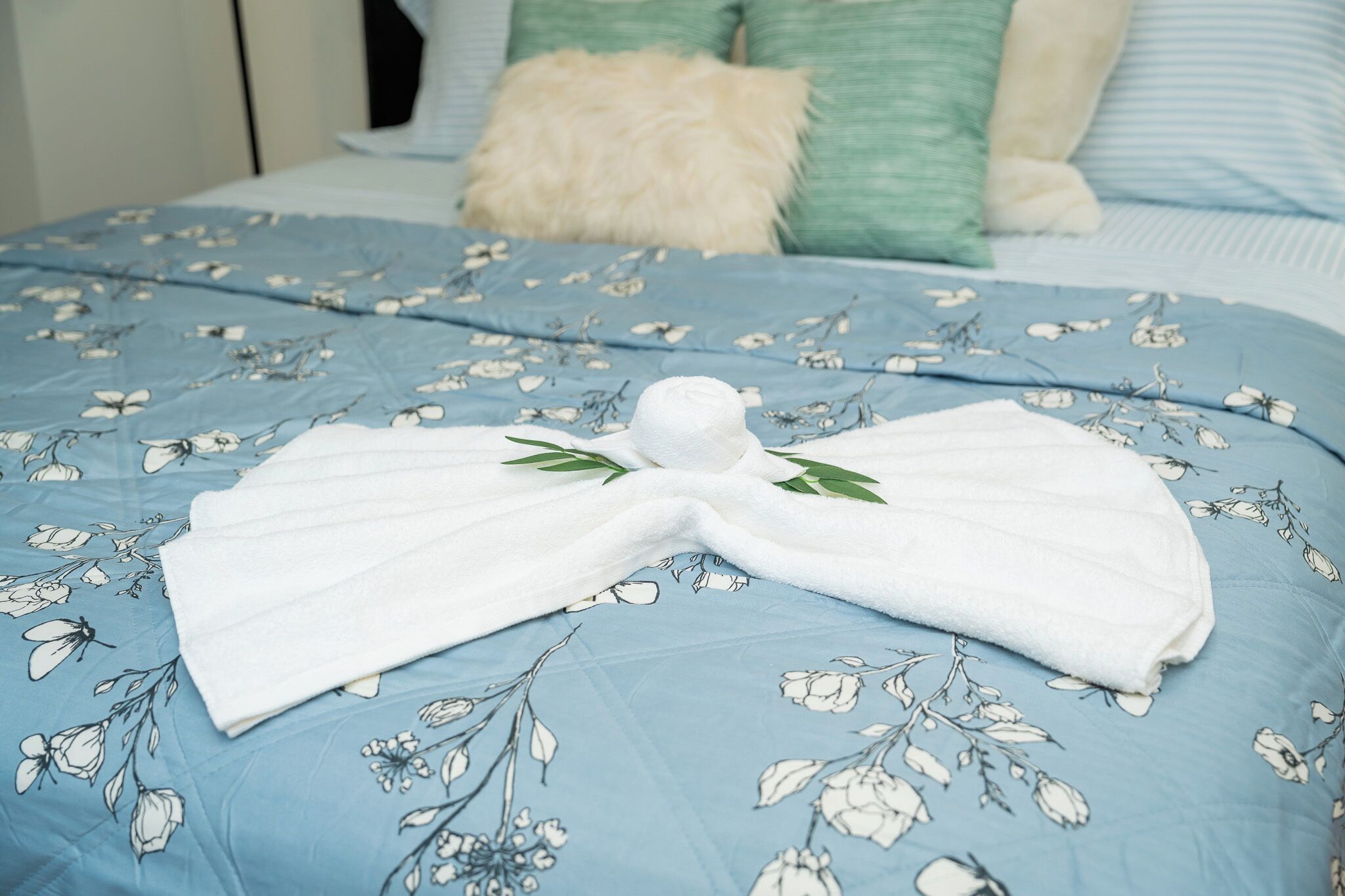Ein ordentlich bezogenes Bett mit einer blau karierten Tagesdecke und einem dazwischen gefalteten weißen Handtuch.