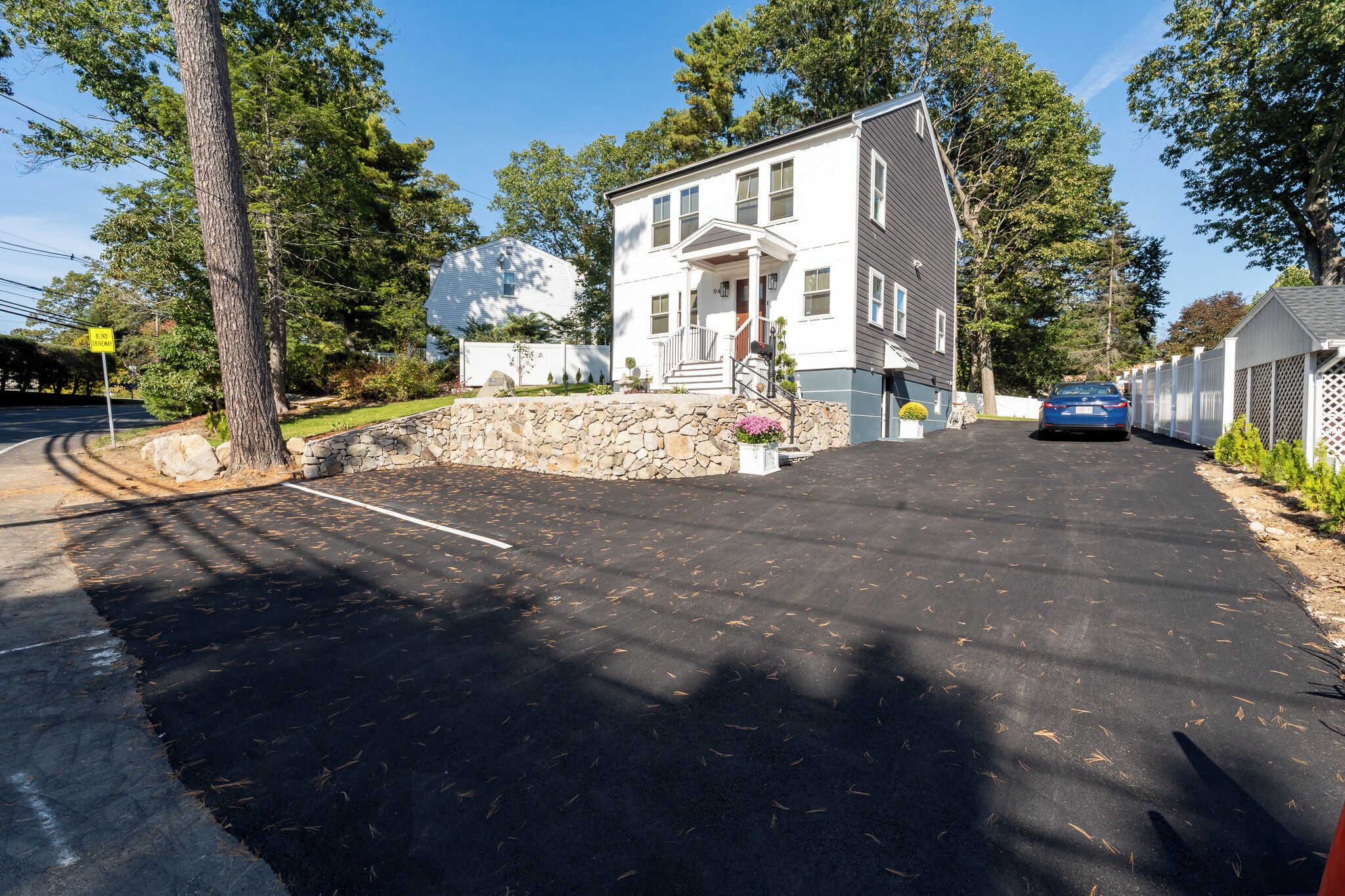 A two-story house with a stone foundation, a front porch, and a driveway leading to a parked car.