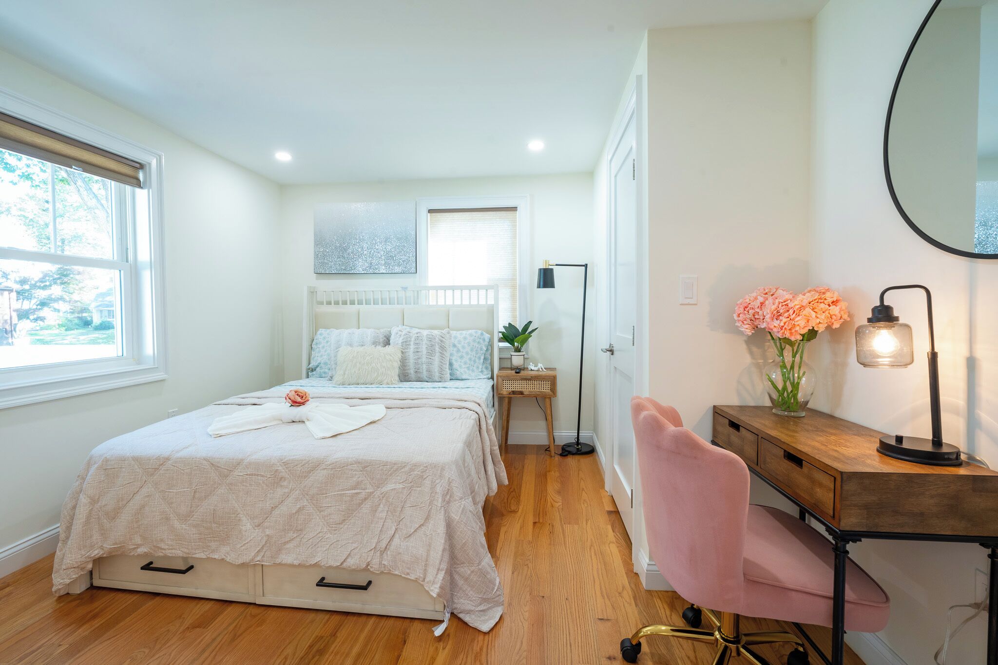 A bedroom with a bed, bedside table, lamp, chair, and a desk with a mirror.