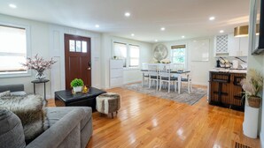 A modern living room with a grey sofa, a coffee table, and a dining area with a white table and chairs. - Elegant 4BR/3BR Home w/Yard & 4 Parking in Dedham (Dedham)