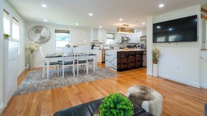 A modern kitchen with a large TV, white cabinets, and a dining area with a table and chairs. - Elegant 4BR/3BR Home w/Yard & 4 Parking in Dedham (Dedham)