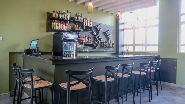 Un espace bar avec un comptoir, de nombreux tabourets et des étagères remplies de bouteilles.