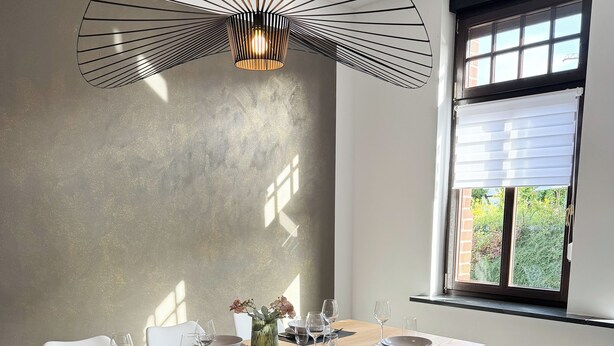 A dining area with a long table set for six, white chairs, a modern pendant light, and a window with blinds. - Beautiful Apartment | Cologne | 15 min. Phantasialand (Hürth)