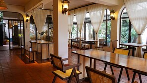 A restaurant with wooden tables and chairs, large windows with curtains, and a tiled floor. - ZZZ Hostel & Restaurant  (Nairobi)