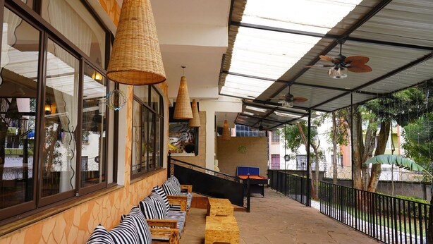 A covered outdoor seating area with wicker lamps, a bed, and a view of the street. - ZZZ Hostel & Restaurant  (Nairobi)