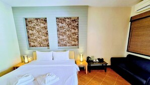 A hotel room with a bed, two wall-mounted lamps, a small table with a lamp, a sofa, and a large window with blinds. - Superior King Room with Sofa & Balcony (Muang Pattaya)