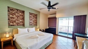 A hotel room with a bed, a ceiling fan, a nightstand, a desk, and a window with curtains. - Superior King Room with Sofa & Balcony (Muang Pattaya)