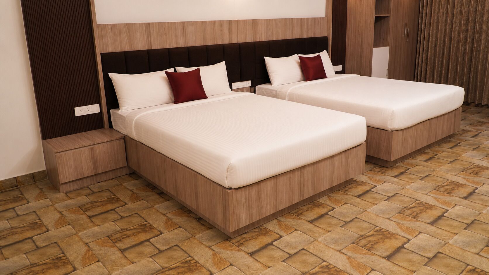 Habitación de hotel con dos camas, cabecero de madera, suelo con diseño de piedra y un armario.