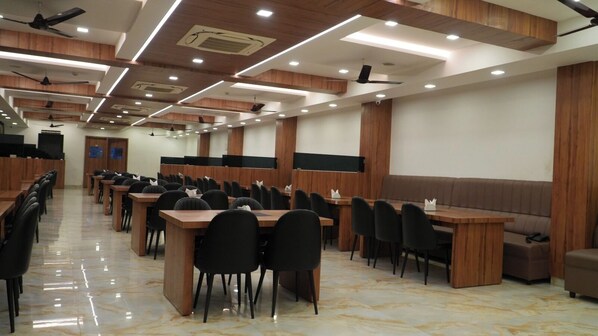 A conference room with multiple tables and chairs, wooden paneling on the walls, and ceiling fans. - Hotel Anitha Parthiban (Thanjavur)