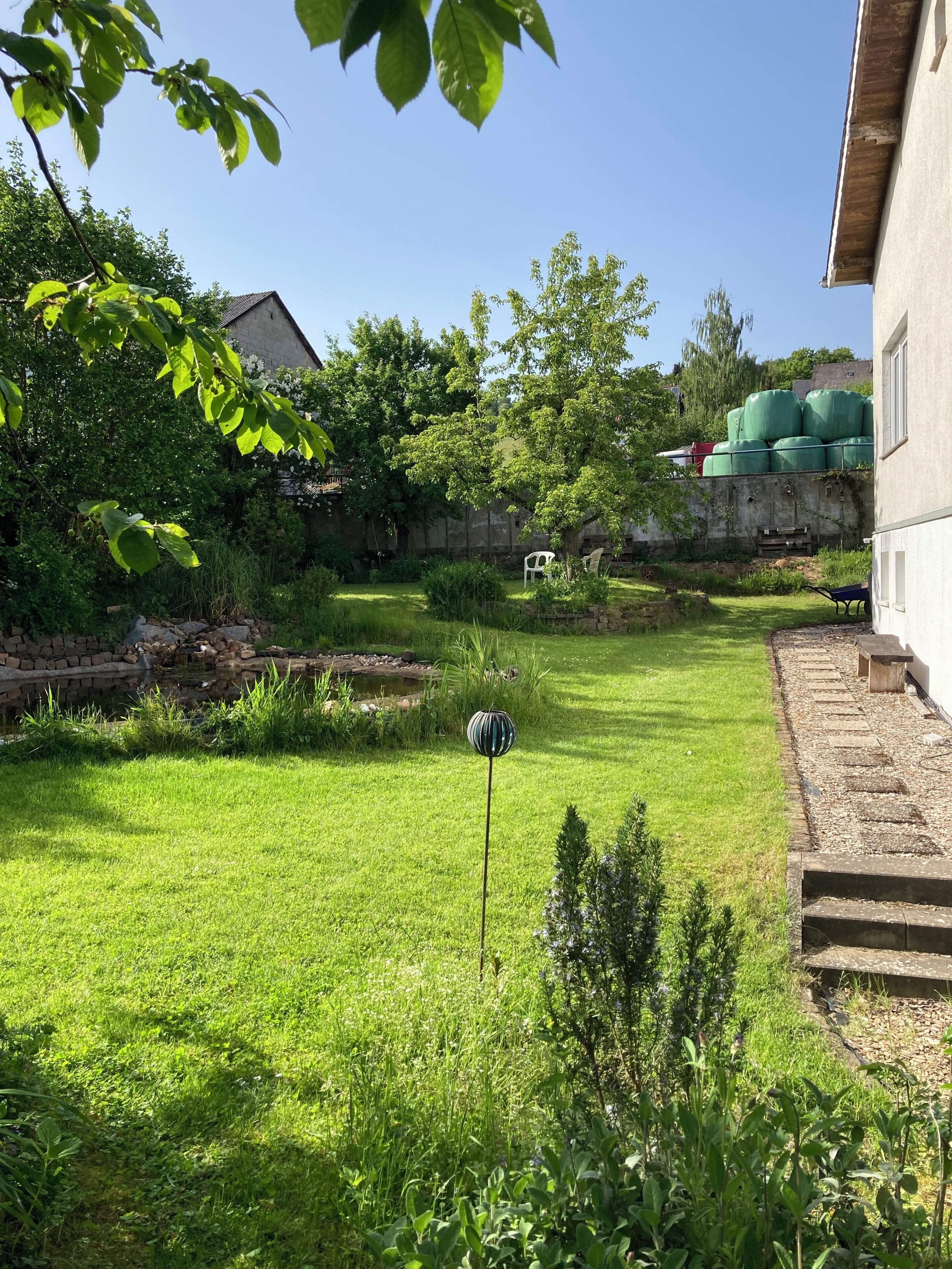 A well-maintained grassy yard with a stone wall, a white chair, and a decorative lamp post.