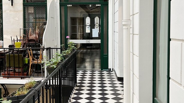 A corridor with a checkered floor, a glass ceiling, and a railing.