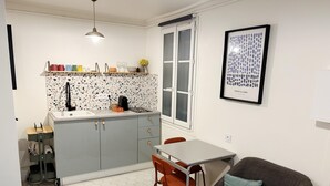 A compact kitchen with a countertop, a sink, and a window. There is a dining table with chairs and a sofa in the living area.