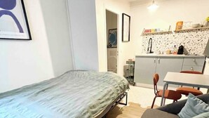 A compact living space with a bed, sofa, kitchenette, and a dining area.