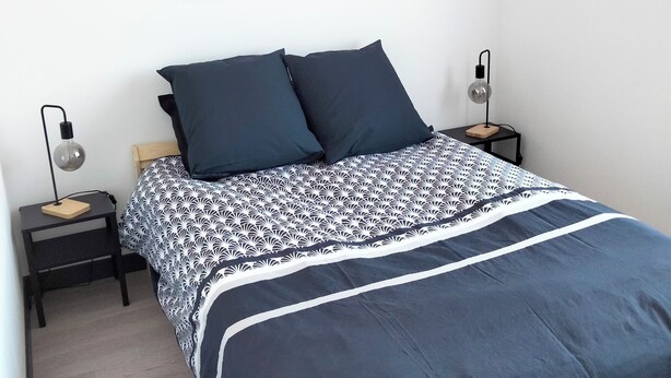 Ein Schlafzimmer mit einem Bett, zwei Nachttischen, einer Wandlampe und einem gerahmten Bild über dem Bett.