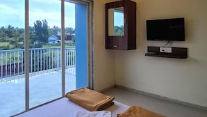 Habitación de hotel con cama, ventilador de techo, televisión y balcón con vistas al exterior.