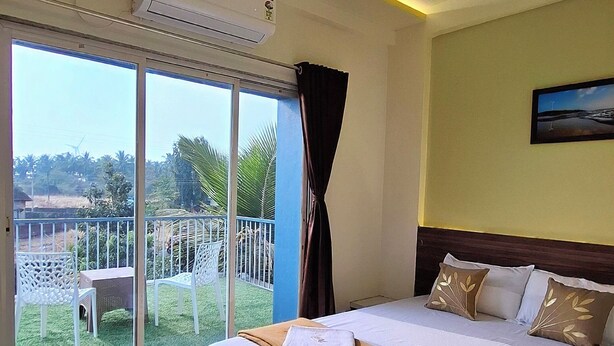 Habitación de hotel con cama, ventilador de techo, ventana grande con cortinas y vista a zonas verdes.