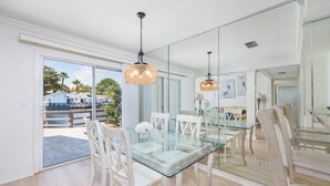 Un espace repas avec une table en verre, des chaises blanches et des lustres en osier suspendus au plafond.