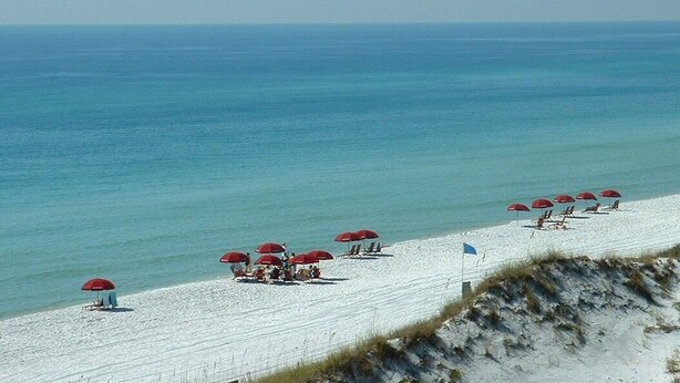 Une plage bordée de rangées de parasols rouges et de sable blanc.