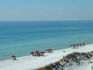 A beach with rows of red umbrellas and white sand.