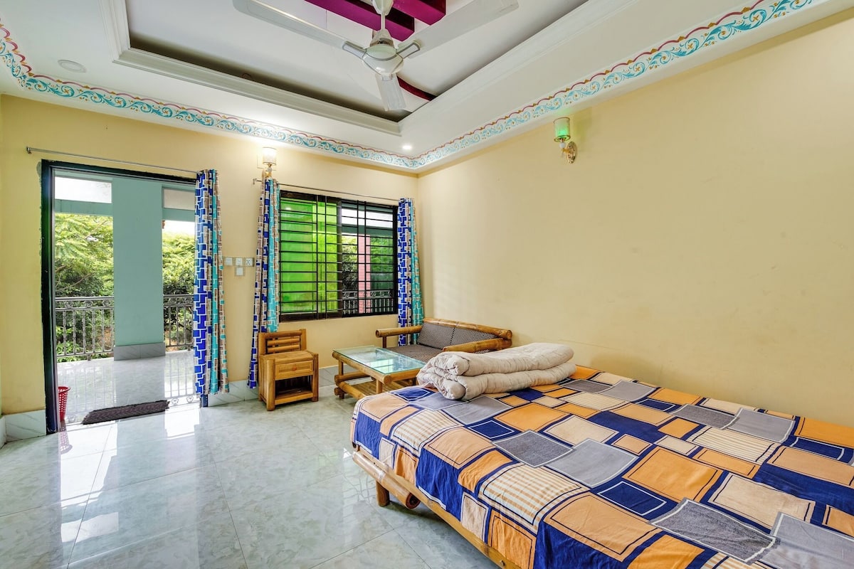 A bedroom with a bed, a small table, a chair, a window with curtains, and a balcony door.