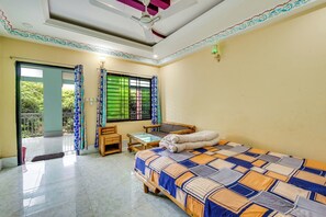 A bedroom with a bed, a small table, a chair, a window with curtains, and a balcony door. - Jaflong Green Resort (Gowainghat)
