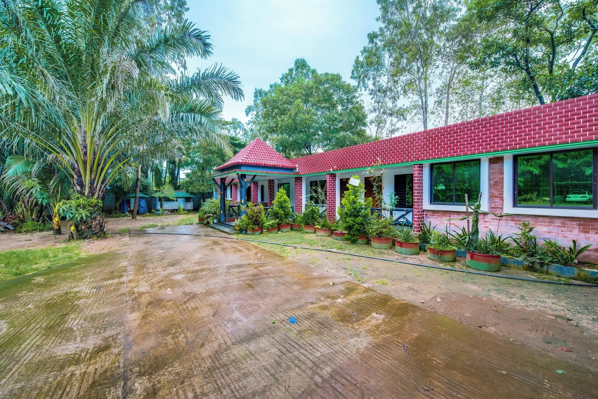 Ein Gebäude aus rotem Backstein mit überdachter Terrasse, umgeben von üppiger Vegetation und Palmen.