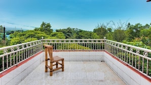 A balcony with a wooden chair, white tiled floor, and a metal railing with decorative elements.
