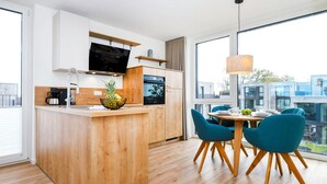 Uma cozinha moderna com ilha de madeira, área de jantar com cadeiras azuis e uma grande janela com vista para a cidade.