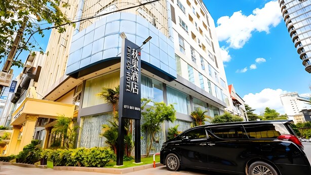 Een modern hotel met een gebogen gevel, een opvallend bord en een zwarte auto voor de deur.