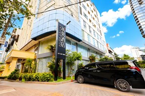 Un hôtel moderne à la façade incurvée, avec une enseigne bien visible et une voiture noire garée devant.