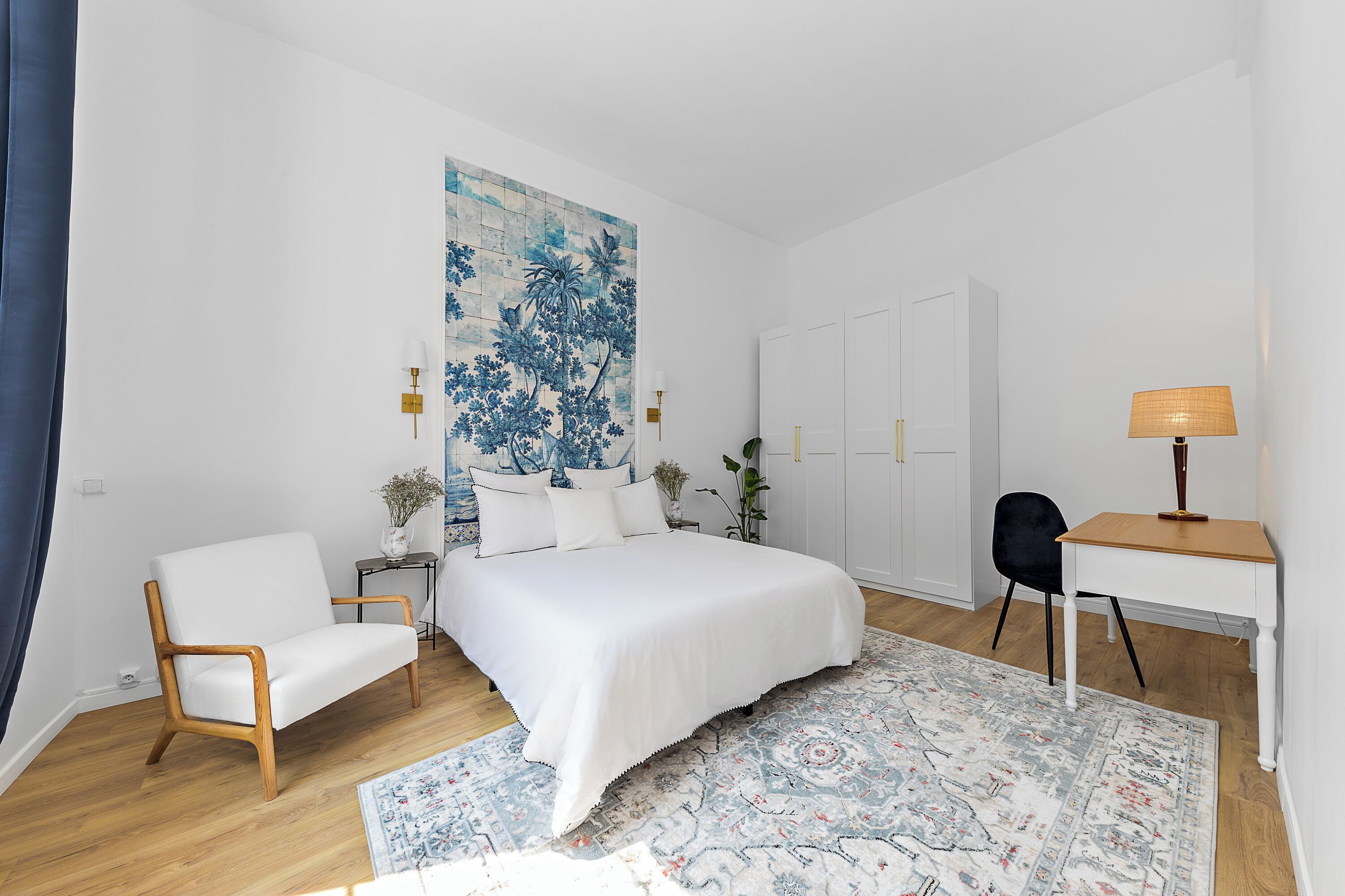 Een slaapkamer met een bed, een stoel, een bureau en een groot schilderij aan de muur.